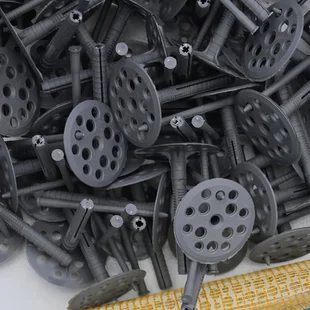 Spezialdübel - Eine Reihe von Bauteilen für die Dämmung von Wänden. Plastikdübel, eine Gitterrolle für die Dämmung von Fassaden und ein Eckprofil mit Gitter liegen auf der Schaumpolystyrol-Oberfläche - Stock-Fotografie